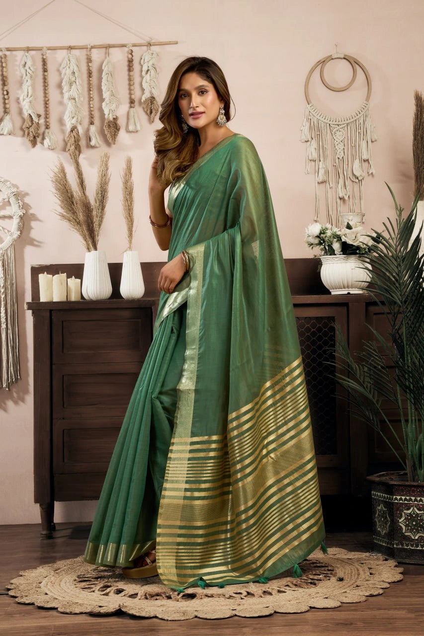 Woman wearing a green saree with a gold border in a decorated room.
